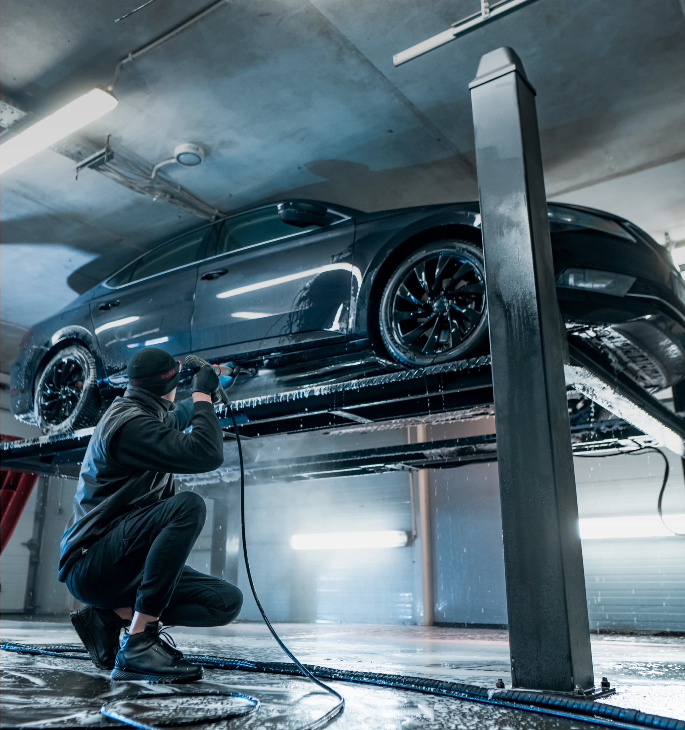 Mężczyzna myjący maszyną ciśnieniową samochód na podnośniku