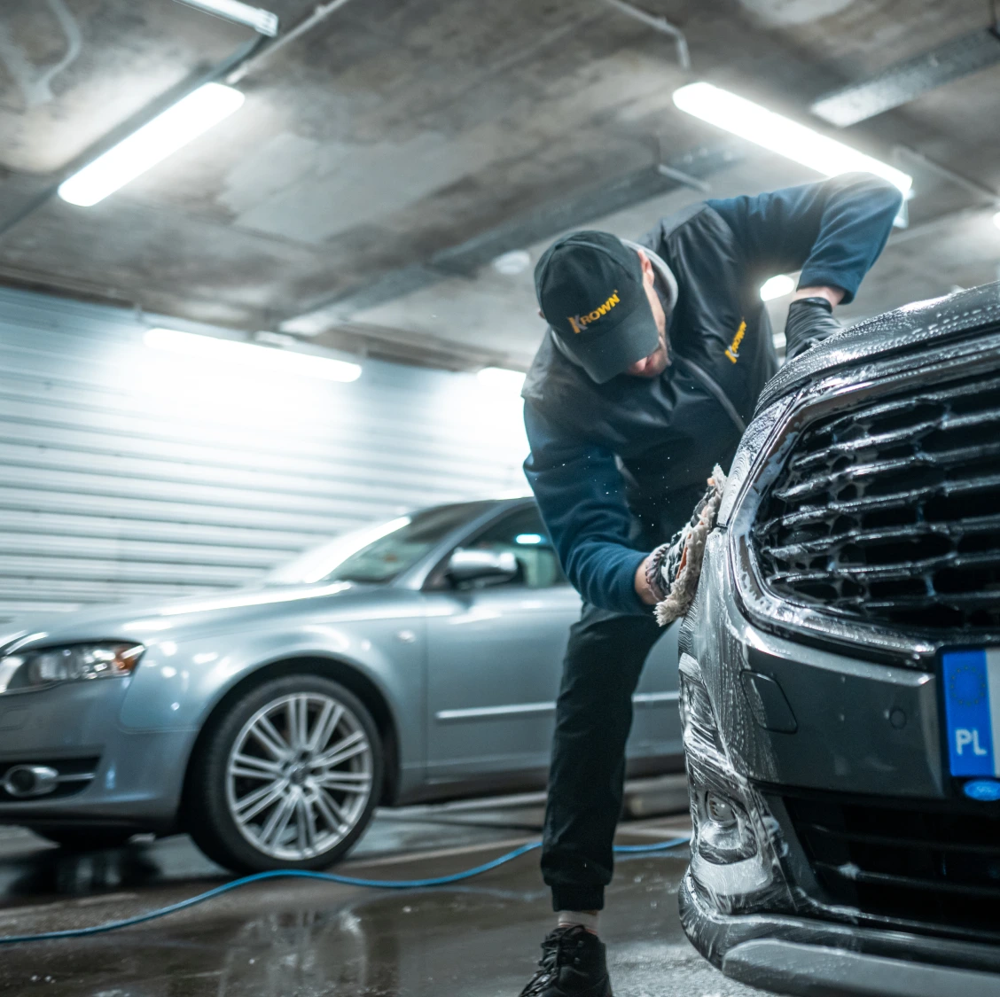 Mężczyzna myjący ręcznie samochód, w tle błyszczący samochód